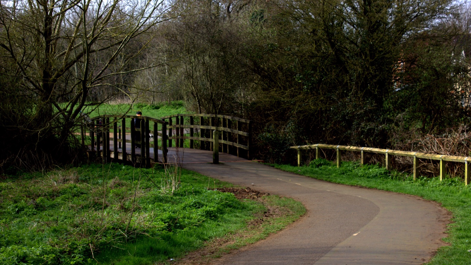 Curving paved footpath leading to a sturdy timber footbridge crossing the River Bure in Bure Park Nature Reserve, photographed in March 2017.