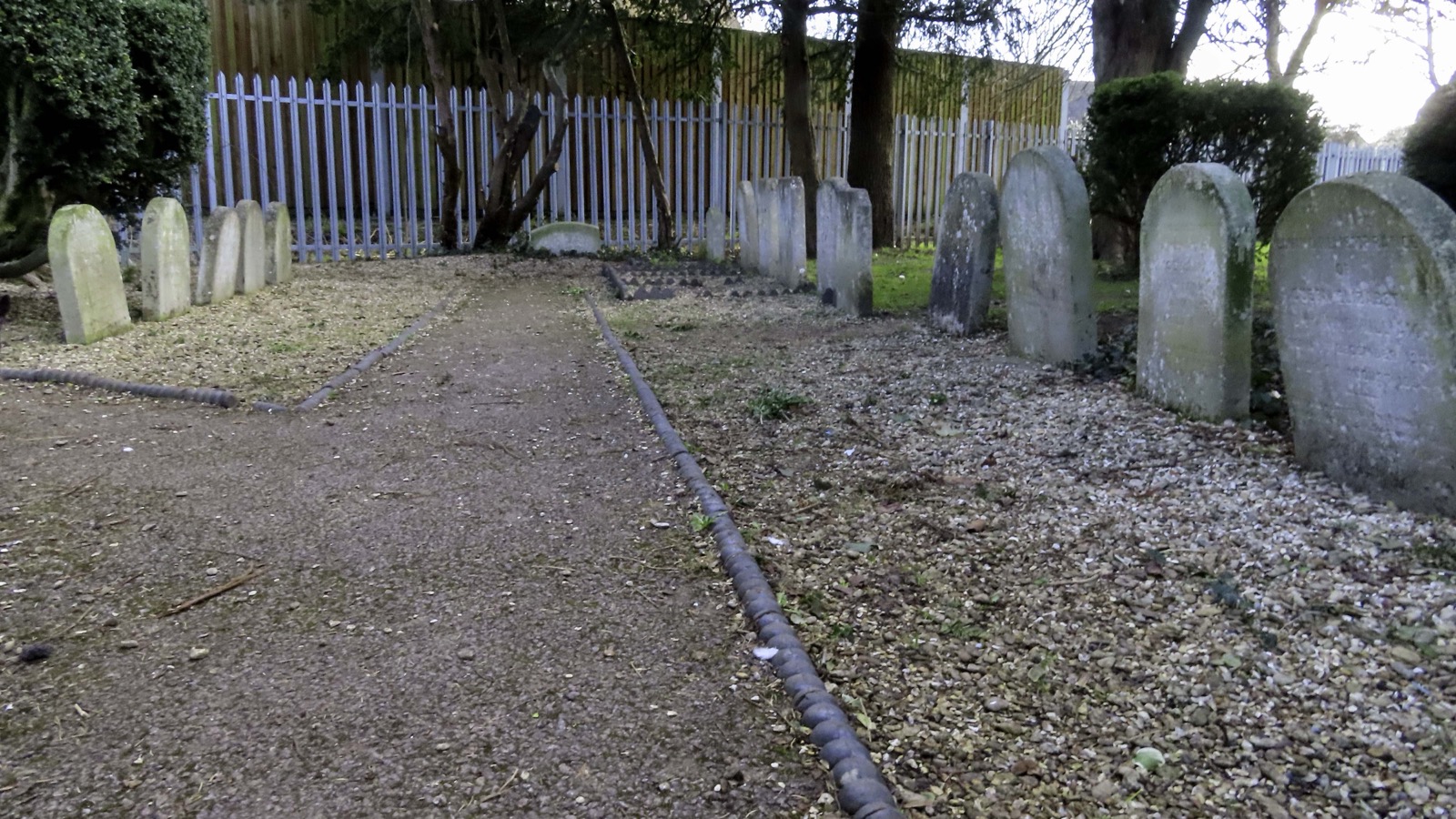Historic Victorian dog gravestones lining a gravel path in a shaded corner of Garth Park, Bicester, photographed in February 2021.