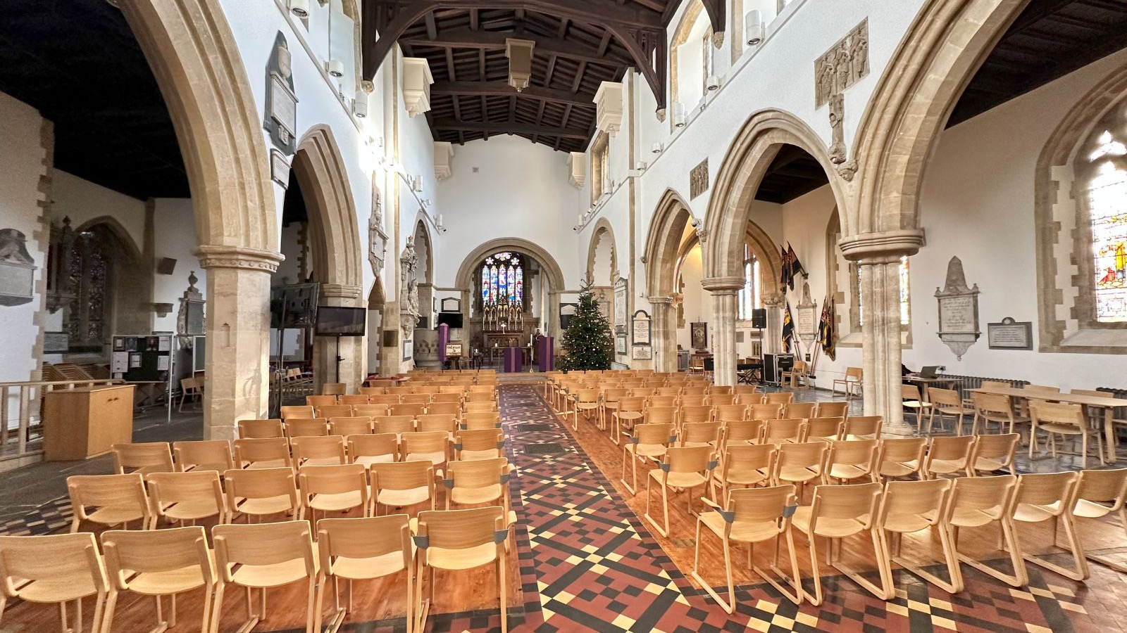 Interior view of St Edburg's Church in Bicester showing the stone nave arcades, timber roof beams, and patterned tile floor, photographed in December 2024.